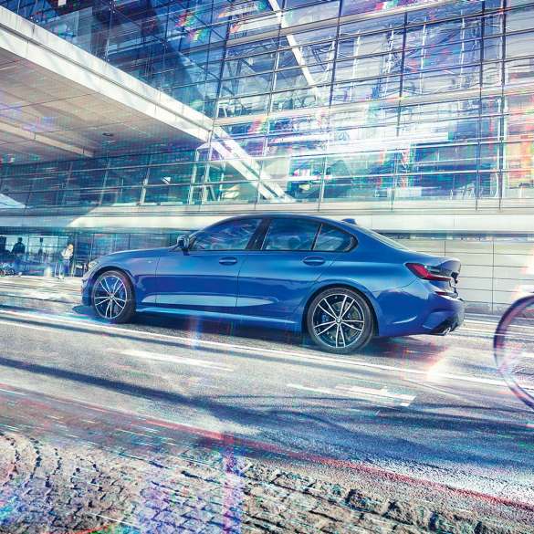 Still shot of the BMW 3 Series Sedan from the side on the day in front of a glass building.