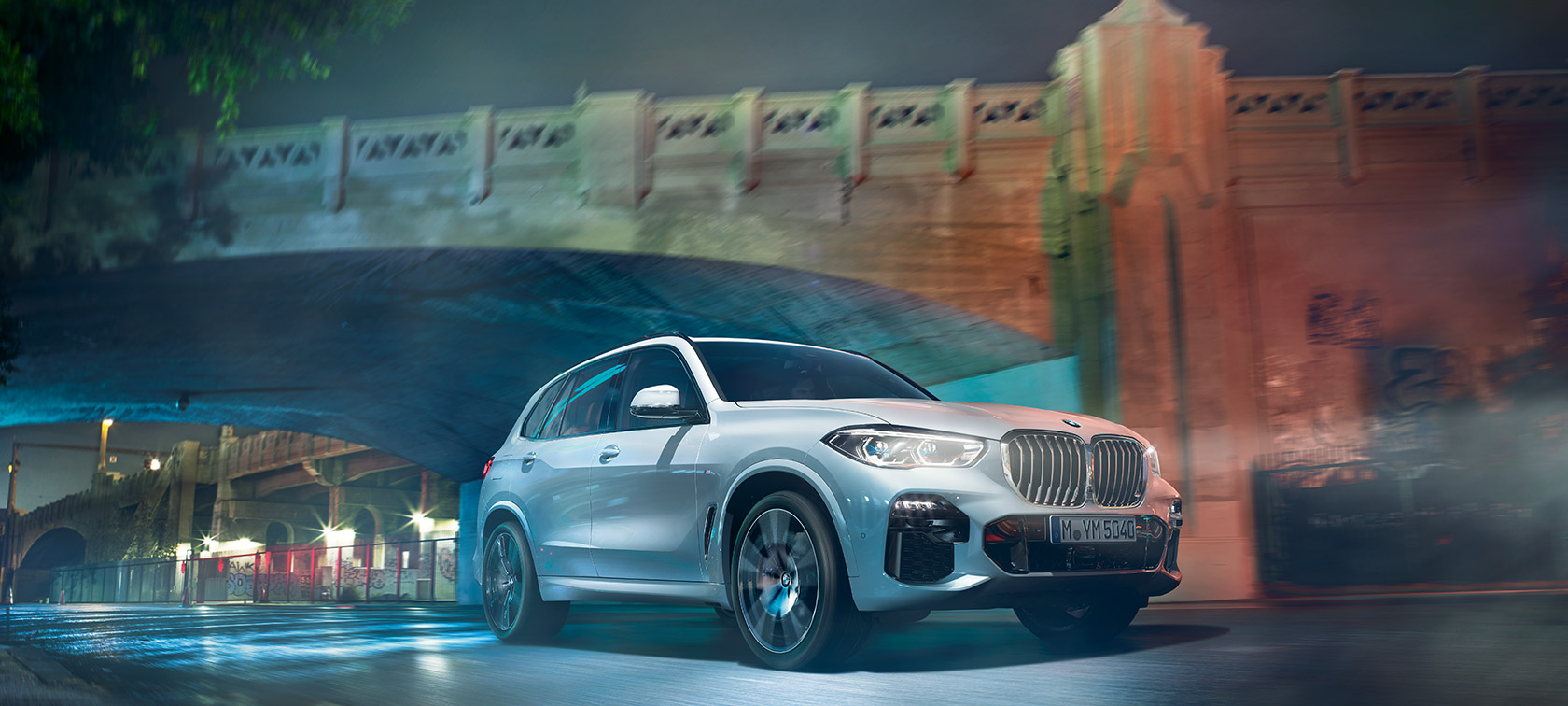 Front view of driving BMW 5 Series Sedan by day under glass building.