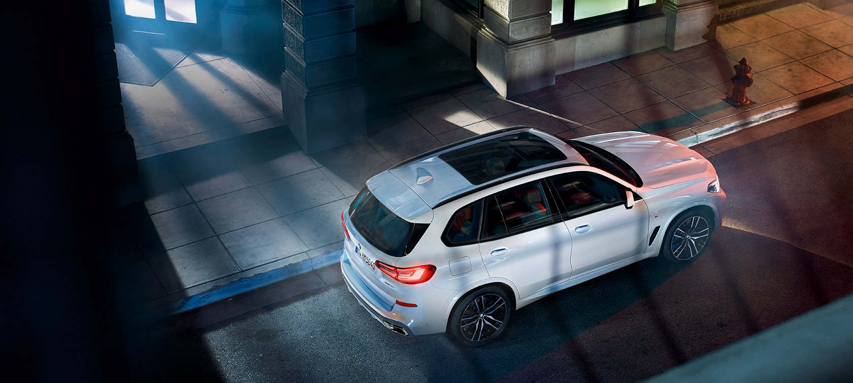 Front view of driving BMW 5 Series Sedan by day under glass building.